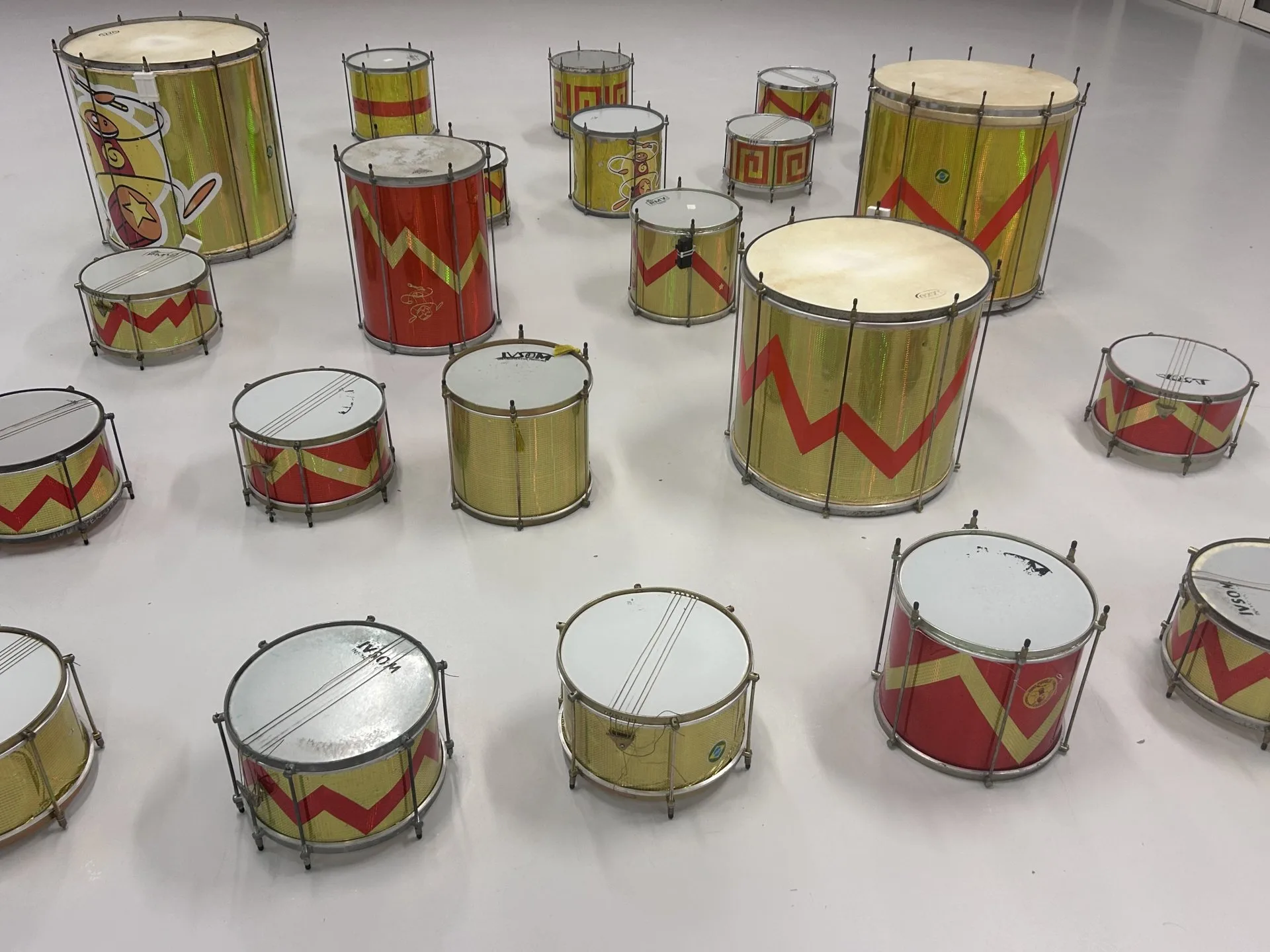 Rangée de surdos et caixas des Percuterreux d'la Beauce, tambours dorés à motifs rouges, posés au sol avant une prestation